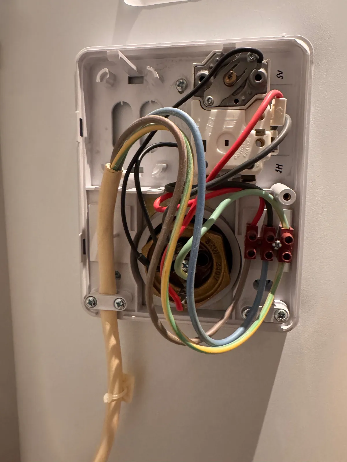 Immersion heater thermostat and wiring exposed behind the cover on the side of a hot water cylinder